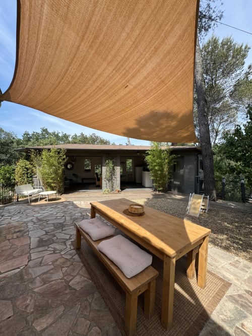 Terrasse extérieure de la villa Domaine d'Olga à Aniane avec table de salle à manger en bois, voile d'ombrage et bâtiment de lodge moderne entouré de