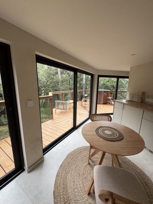 Salle à manger de villa moderne avec table ronde en bois surplombant une terrasse en bois et la forêt au Domaine d'Olga, Aniane
