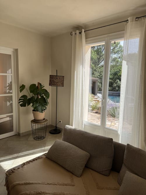 Séjour lumineux avec canapé gris, plante monstera en pot, lampadaire et portes vitrées donnant sur le jardin du Domaine d'Olga