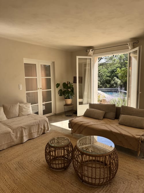 Séjour lumineux du Domaine d'Olga avec mobilier beige, vue sur jardin par portes vitrées et tables d'appoint en osier