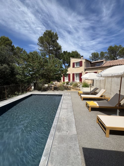 Zone piscine de la villa Domaine d'Olga à Aniane avec transats, parasol et maison aux volets rouges