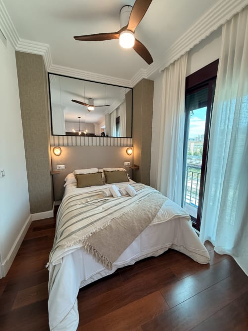 Dormitorio moderno en Sinese Design Homes en Málaga con vistas a la ciudad, ropa de cama a rayas, ventilador de techo y acceso a balcón