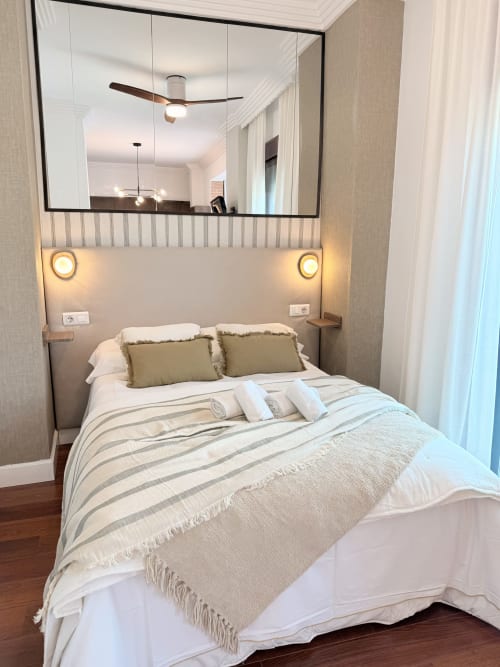 Moderno dormitorio de estudio en Málaga con cama queen, ropa de cama rayas, almohadas oliva, cabecero iluminado, espejo grande y