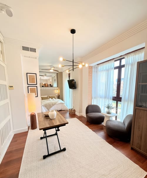 Moderno estudio en Málaga con sala diáfana, dormitorio, comedor, sillones grises, mesa de madera y vistas a la ciudad