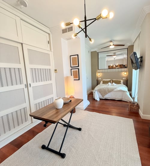 Luminoso apartamento estudio moderno en Málaga con suelos de madera, armarios empotrados blancos, iluminación colgante contemporánea y