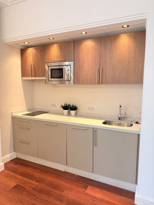 Cocina moderna con muebles altos de madera, armarios inferiores claros, fregadero y microondas de acero inoxidable en apartamento de Málaga