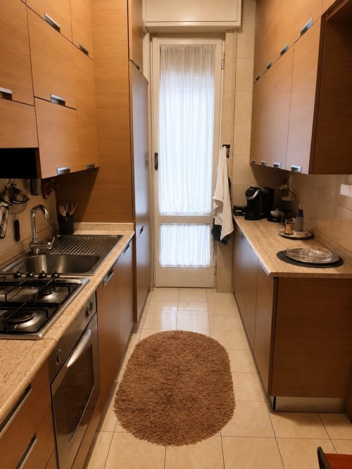 Modern galley kitchen in Roma apartment with wood cabinets, gas stove, and beige tile flooring