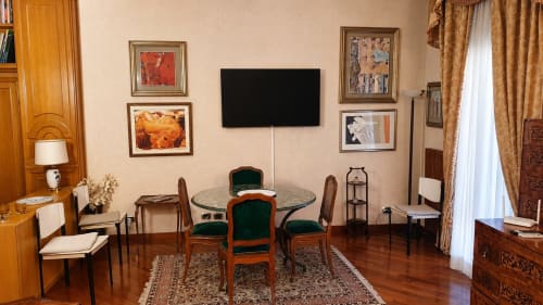 Elegant Roman apartment living area with round dining table, green velvet chairs, framed artwork, flat-screen TV, and wooden