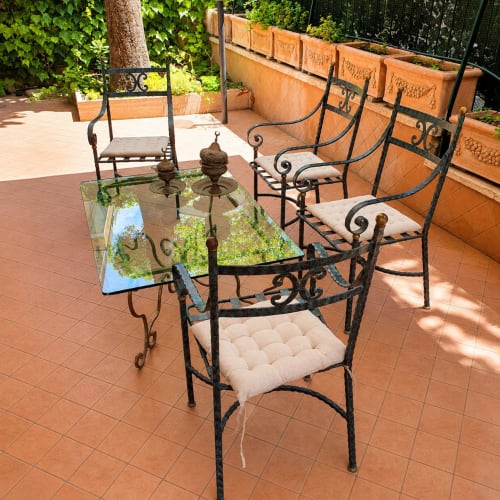 Elegant wrought iron seating and glass table on terracotta terrace at Roma apartment House Mary Grace with lush garden