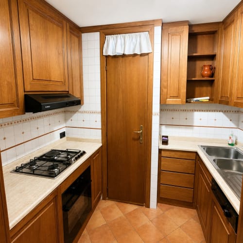 Cucina compatta con mobiletti in legno, fornello a gas e rivestimento in piastrelle bianche nella residenza Altipiani di Arcinazzo