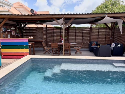 Espace piscine de l'hôtel Kay Lakansiel au Vauclin avec zone lounge couverte, chaises en bois et bacs de rangement colorés