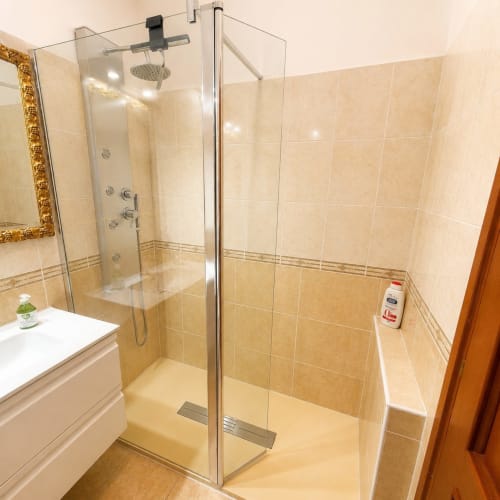 Modern shower enclosure in Roma apartment with beige tiles, rainfall showerhead, and glass doors at Myob property