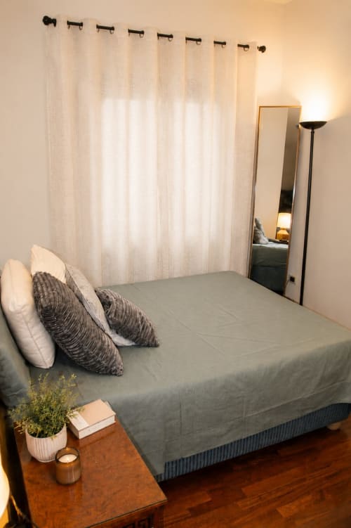 Modern bedroom at Myob apartment in Rome featuring gray bed, white curtains, mirror, and wooden nightstand