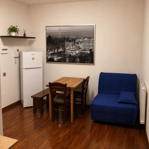Cozy Roma apartment with dining table, blue sofa, white fridge, and Eiffel Tower night view in framed print.