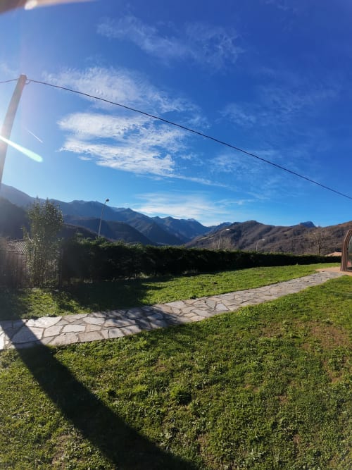 Exuberante jardín verde y patio de Casa Rural Posada Real en Pajares con vistas a la montaña y cielo azul