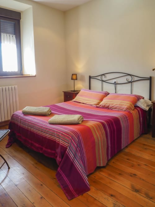 Dormitorio con ropa de cama a rayas coloridas y cama de hierro forjado en la casa rural Posada Real, Pajares, España
