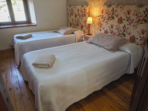 Camas gemelas con sábanas blancas en casita rural de Casa Rural Posada Real de Pajares, España, con papel tapiz floral