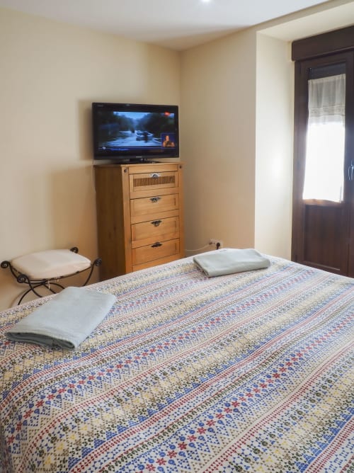 Acogedora habitación en Casa Rural Posada Real de Pajares con ropa de cama estampada, cómoda de madera, TV de pantalla plana y vistas a las montañas