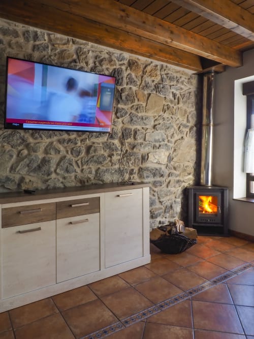 Acogedora sala de estar de casa rural con chimenea de piedra, vigas de madera, TV de pantalla plana y estufa de leña activa en Casa Rural Posada Real
