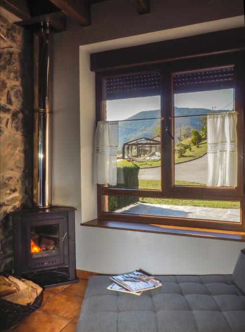 Acogedora habitación de Casa Rural Posada Real con chimenea, vistas a las montañas a través de grandes ventanales y cómoda zona de estar