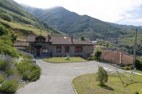 Casa Rural Posada Real de Pajares, villa de montaña con fachada de piedra, jardín, hamacas y vistas al verde valle asturiano.