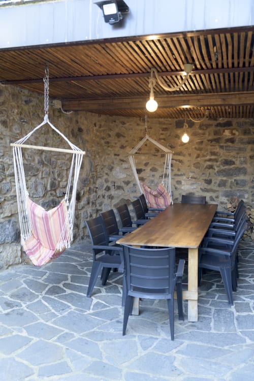 Porche cubierto con mesa de madera, sillas negras y hamacas de rayas rosas en Casa Rural Posada Real de Pajares