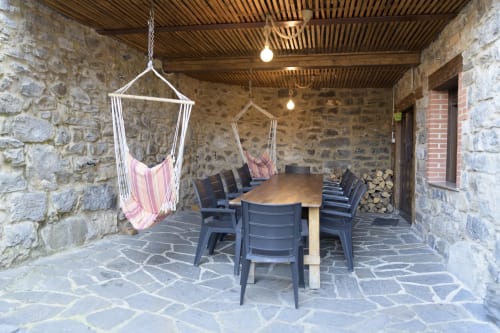 Porche cubierto con mesa de comedor, sillas, hamaca rosa y muros de piedra en Casa Rural Posada Real de Pajares