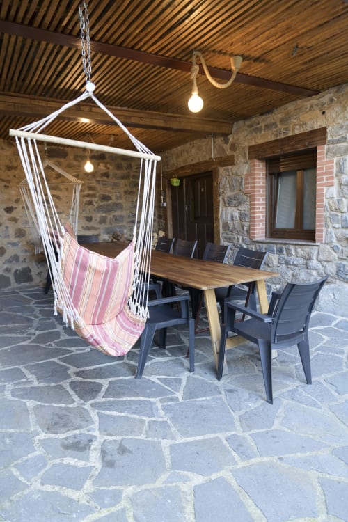 Silla hamaca de rayas rosas en patio de piedra de Casa Rural Posada Real de Pajares, con mesa de comedor y vistas a las montañas
