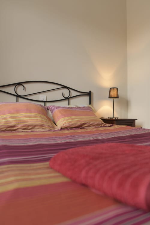 Ropa de cama a rayas de colores en cama de hierro forjado con lámpara de noche en la habitación de Casa Rural Posada Real de Pajares