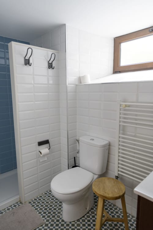 Baño moderno con azulejos blancos tipo metro en las paredes, inodoro, toallero climatizado y banqueta de madera en Casa Rural Posada Real de