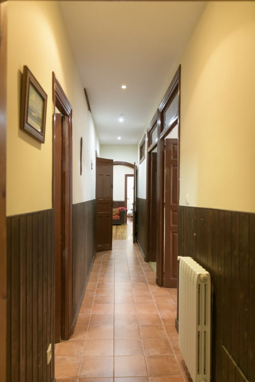 Pasillo de la Casa Rural Posada Real de Pajares con puertas de madera, suelo de baldosa de barro y paredes amarillas con zócalo oscuro