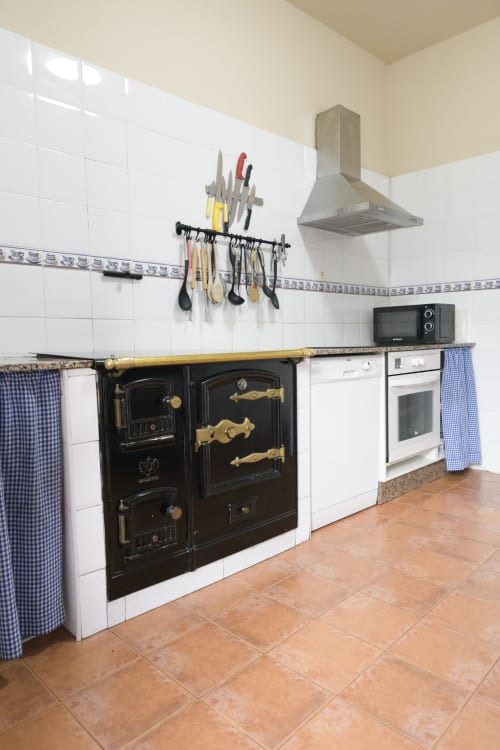Cocina rústica en Casa Rural Posada Real de Pajares con estufa vintage negra, azulejos blancos, campana de cobre y utensilios
