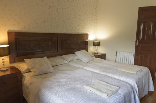 Dormitorio con cabecero de madera ornamentado, camas gemelas con colchas estampadas, lámparas de noche y vistas a la montaña en Casa Rural