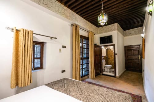 Chambre deluxe du Riad Fes Aicha à Fès avec lit, portes en bois, rideaux dorés et décoration marocaine traditionnelle