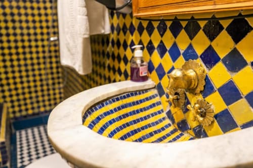 Lavabo orné avec carrelage marocain jaune et bleu au Riad Fes Aicha à Fès, Maroc