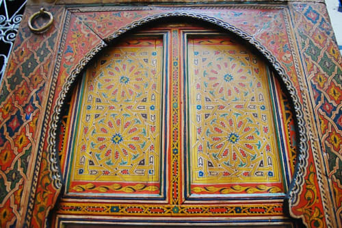Porte cintrée ornée de motifs géométriques islamiques en or, rouge et bleu au Riad Fes Aicha, Fès