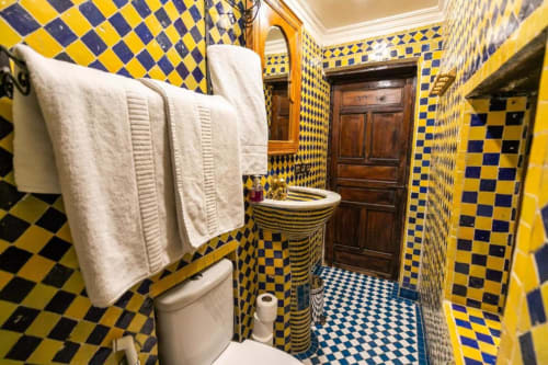 Salle de bain carrelée bleu et jaune du Riad Fes Aicha avec lavabo, toilettes et serviettes blanches, Fès Maroc