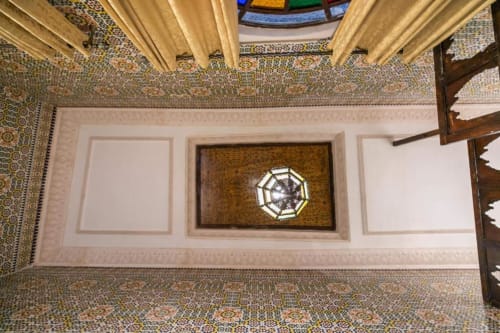 Vue de dessus d'une chambre de riad marocain ornée avec plafond mosaïqué, rideaux crème et carreaux de zellige géométrique au Riad Fès