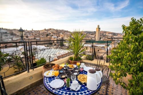 Terrasse petit-déjeuner sur le toit du Riad Fes Aicha avec cuisine marocaine, table aux motifs bleus et vue sur la médina de Fès