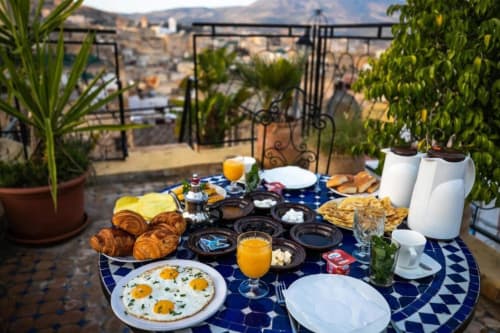 Petit-déjeuner sur le toit du Riad Fes Aicha avec œufs, croissants, jus d'orange et vue sur la médina de Fès.
