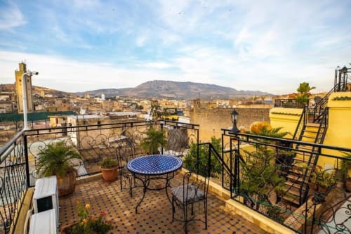 Terrasse du Riad Fes Aicha avec table en mosaïque bleue surplombant la médina de Fès et les montagnes, Maroc