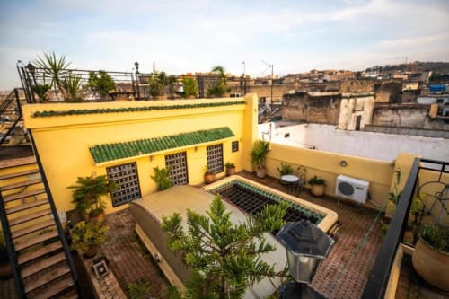 Terrasse sur le toit du Riad Fes Aicha à Fès avec murs jaunes, plantes et vue sur la médina
