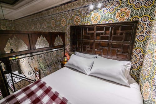 Chambre de style marocain au Riad Fes Aicha avec murs en zellige, tête de lit sculptée et literie blanche