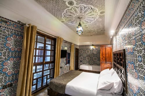 Chambre ornée du riad Fes Aicha à Fès avec zellige traditionnel, portes en bois sculpté et plafond décoratif