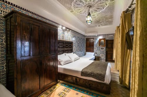 Chambre de luxe du Riad Fes Aicha avec zellige marocain traditionnel, lit en bois ouvragé et rideaux dorés à Fès