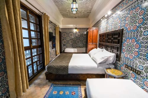 Chambre du Riad Fes Aicha avec zellige bleu ornementé, lits en bois, porte cintrée et décor marocain traditionnel à Fès