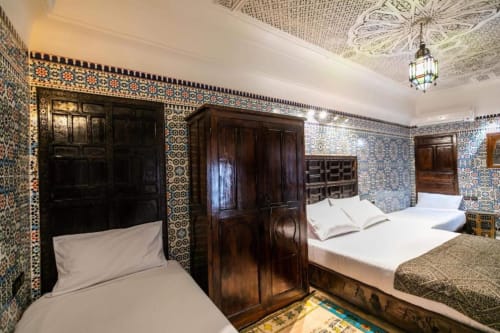 Chambre du Riad Fes Aicha à Fès avec zellige ornementé, mobilier en bois sombre et décor marocain traditionnel
