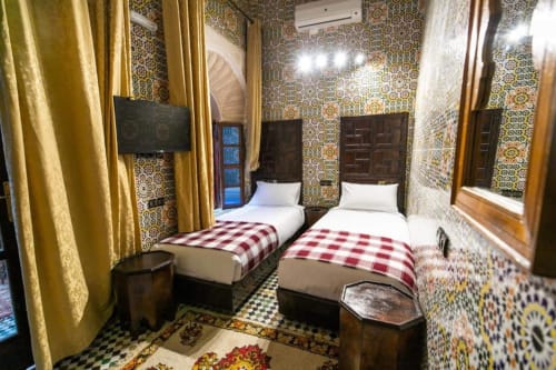 Chambre double avec carrelage zellige marocain traditionnel, rideaux dorés et couvertures écossaises rouges au Riad Fes Aicha à Fès