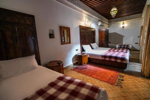 Chambre spacieuse du Riad Fes Aicha à Fès avec plusieurs lits, décor marocain traditionnel, carrelage en terre cuite et bois