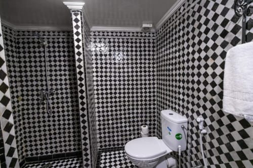 Salle de bains au carrelage damier noir et blanc avec toilettes et douche au Riad Fes Aicha à Fès, Maroc